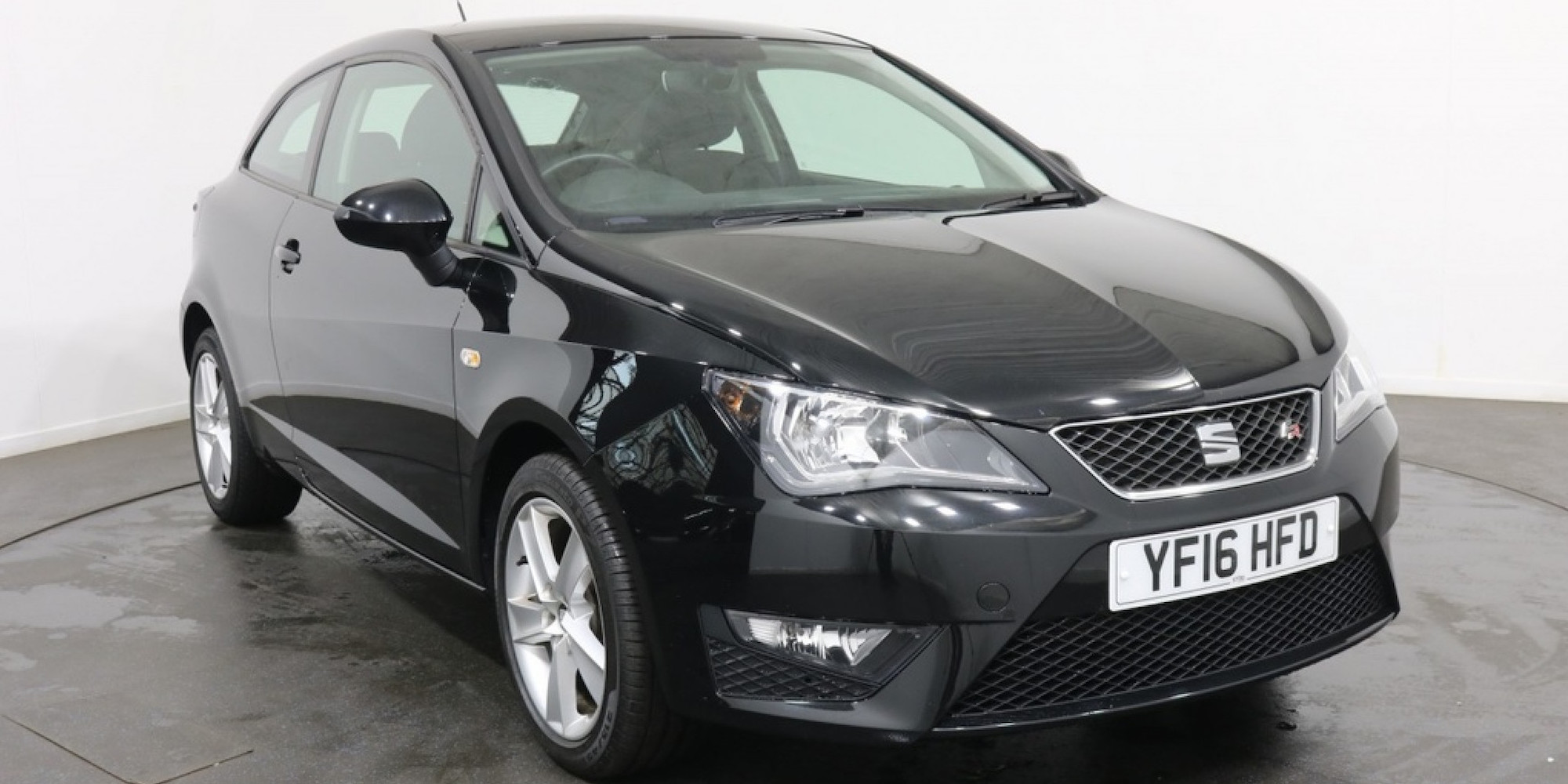 Black SEAT Ibiza parked in showroom, facing three-quarters right